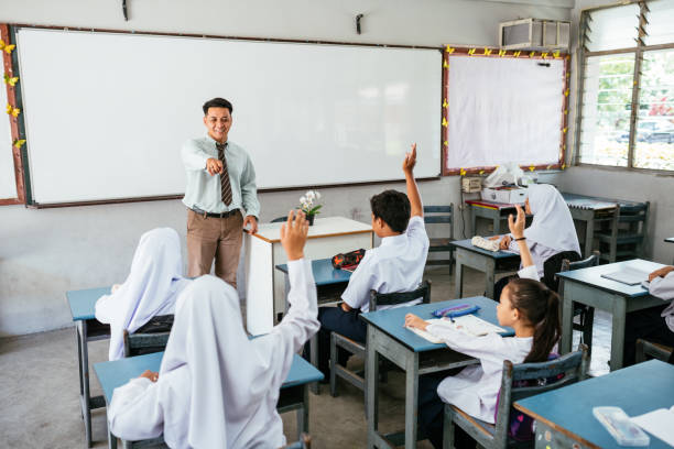 primary school and pupils in classroom. elementary students doing exam and being supervised by male teacher - 教育 個照片及圖片檔